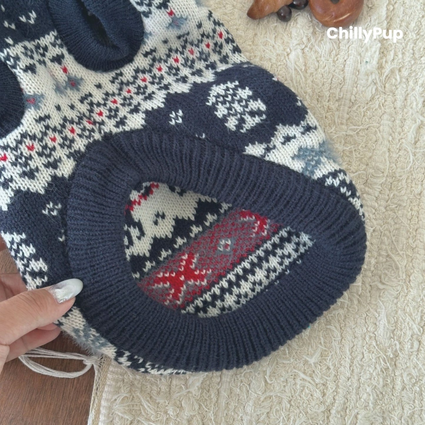 Knitted dog sweater with a pattern of a dog and fish, held by a hand on a textured surface.