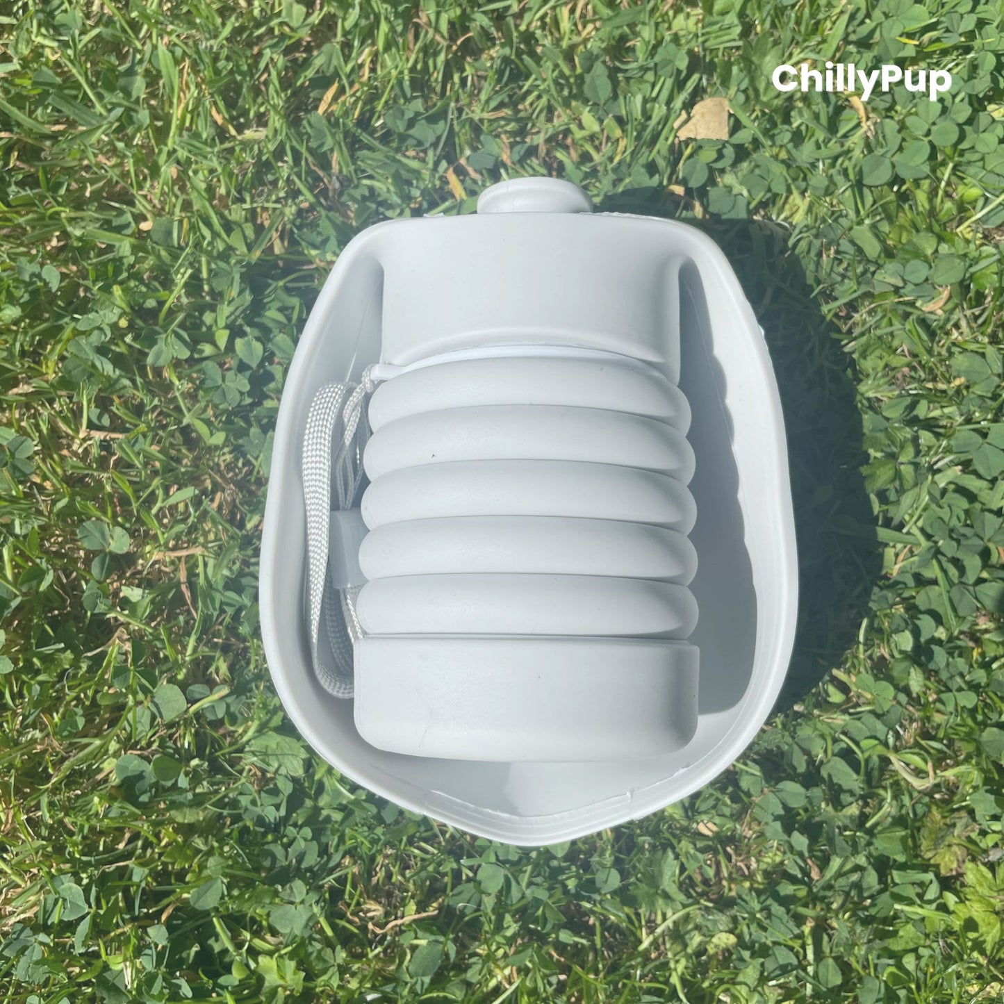 One foldable silicone water bottle completely folded up on grass.