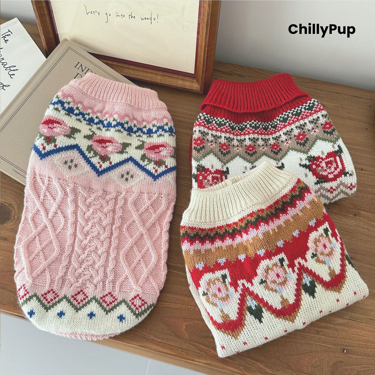 Knitted dog jumpers, one pink and one red with patterns, on a wooden surface with 'ChillyPup' branding.