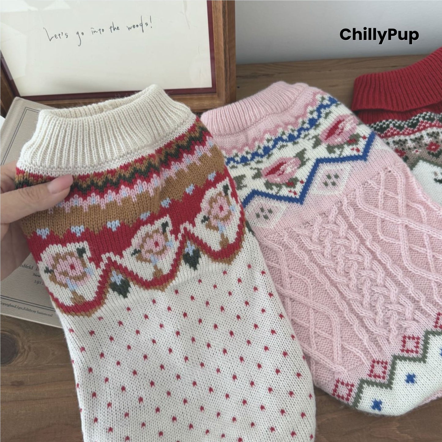 Knitted dog jumpers, one pink and one red with patterns, on a wooden surface with 'ChillyPup' branding.