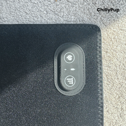 Close-up of a black textured redlight pet mat with a stitched border and an oval control panel featuring white icons, placed on a grey carpet. The ChillyPup brand logo is visible in the top right corner.