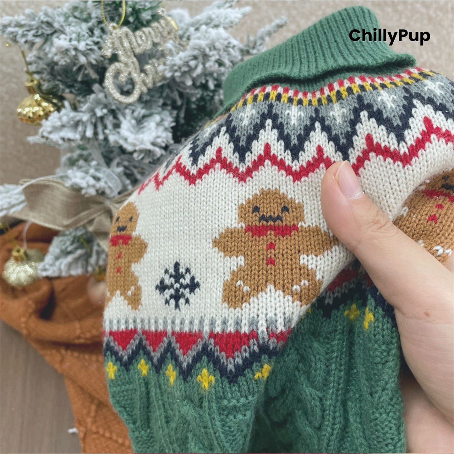 Knitted dog sweater with gingerbread design held by a hand, Christmas tree in the background