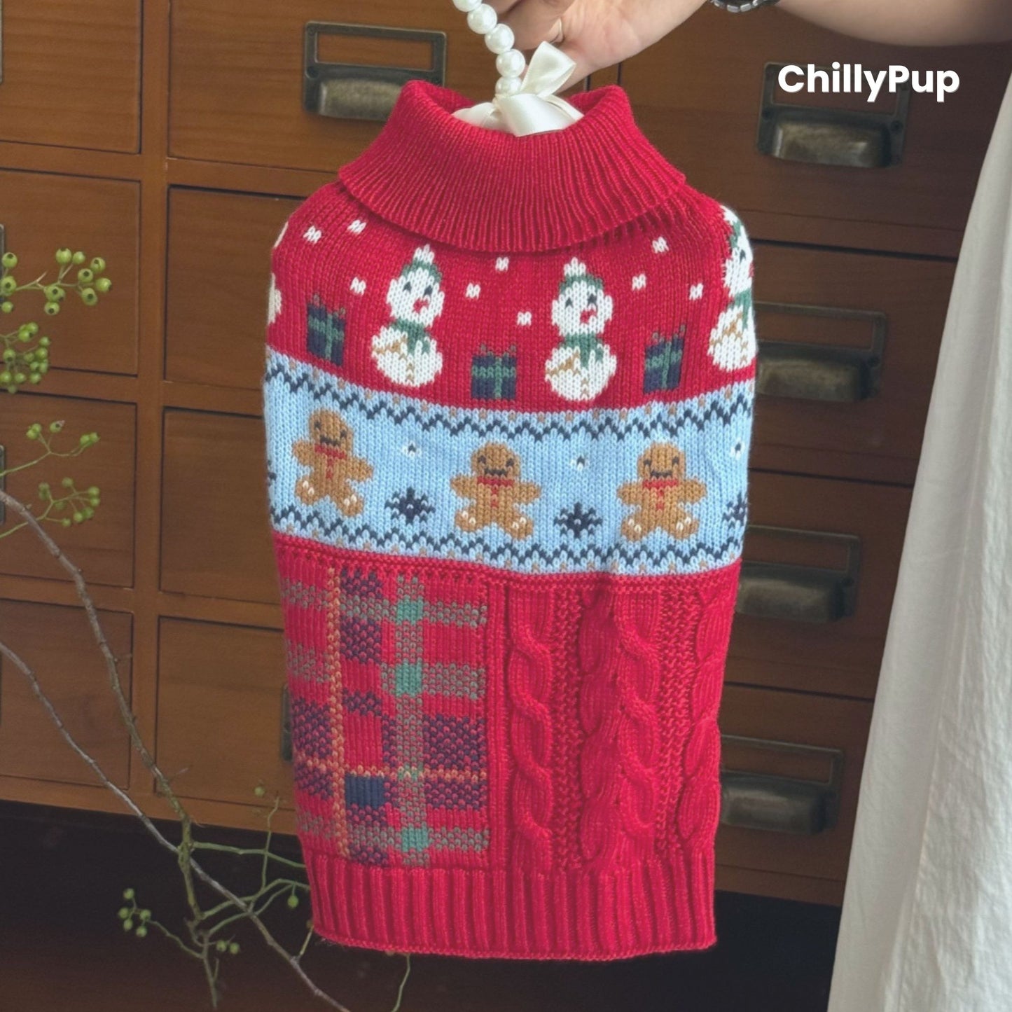 Knitted dog sweater with Christmas design on a wooden surface, surrounded by festive decor. branded with ChillyPup.