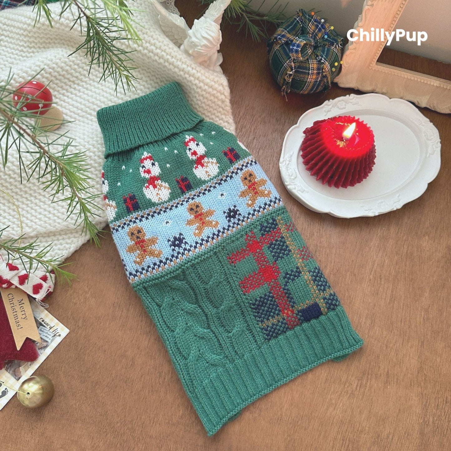 Knitted dog sweater with Christmas design on a wooden surface, surrounded by festive decor. branded with ChillyPup.