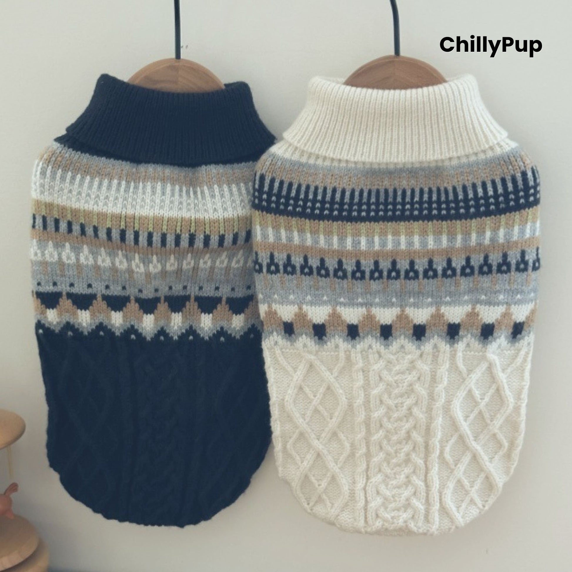 Two dog sweaters, one navy and one white with patterned designs, on hangers against a plain background.